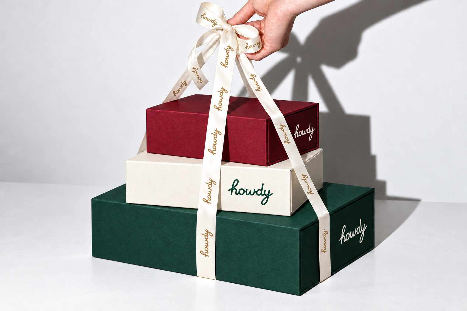 Three Howdy gift boxes in forest green, ivory, and burgundy